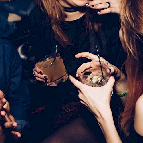 People socializing, holding drinks and laughing in a dimly lit bar or club setting.