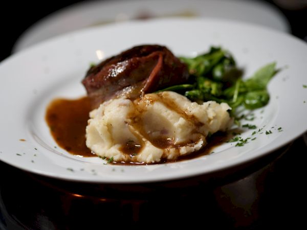 A plate with mashed potatoes, a piece of meat, gravy, and greens.